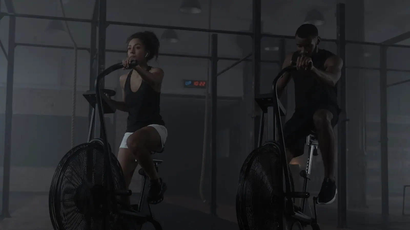 Two riders holding a prescribed output, lit low in a smoke-hung room.
