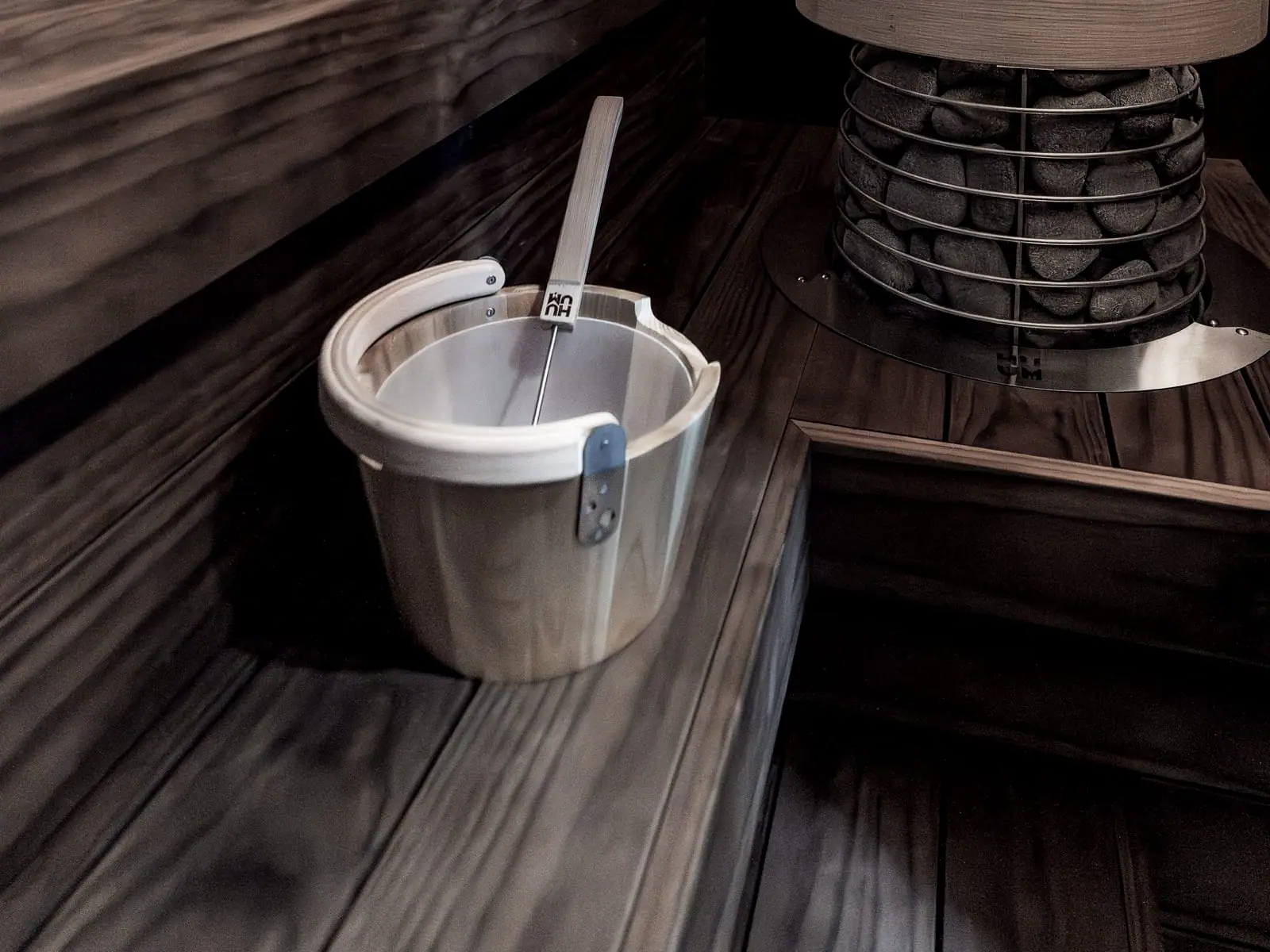 A sauna bucket and ladle on the bench, the stone heater behind.