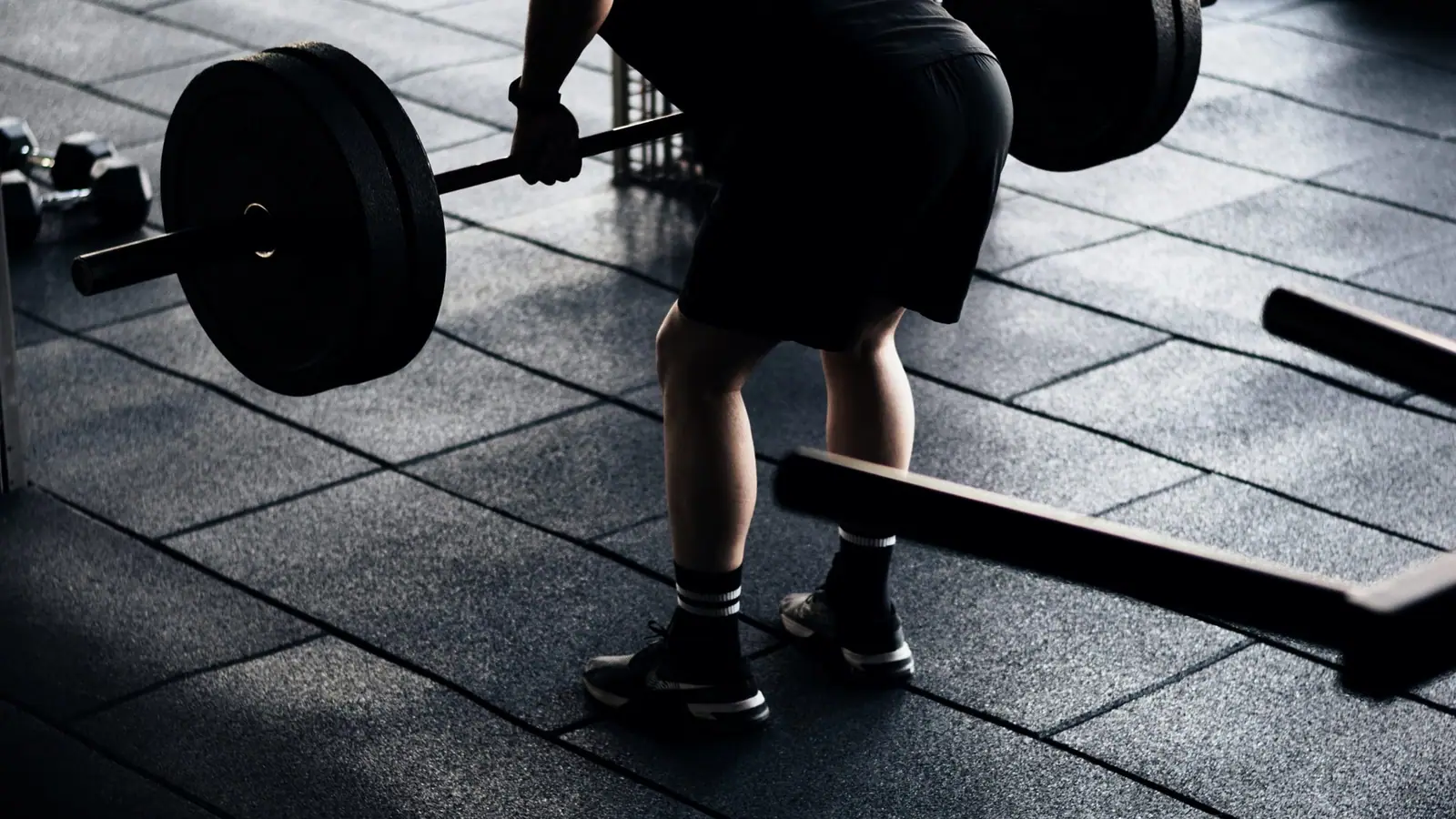 A lifter mid-set under one hard side light, deep shadow behind.